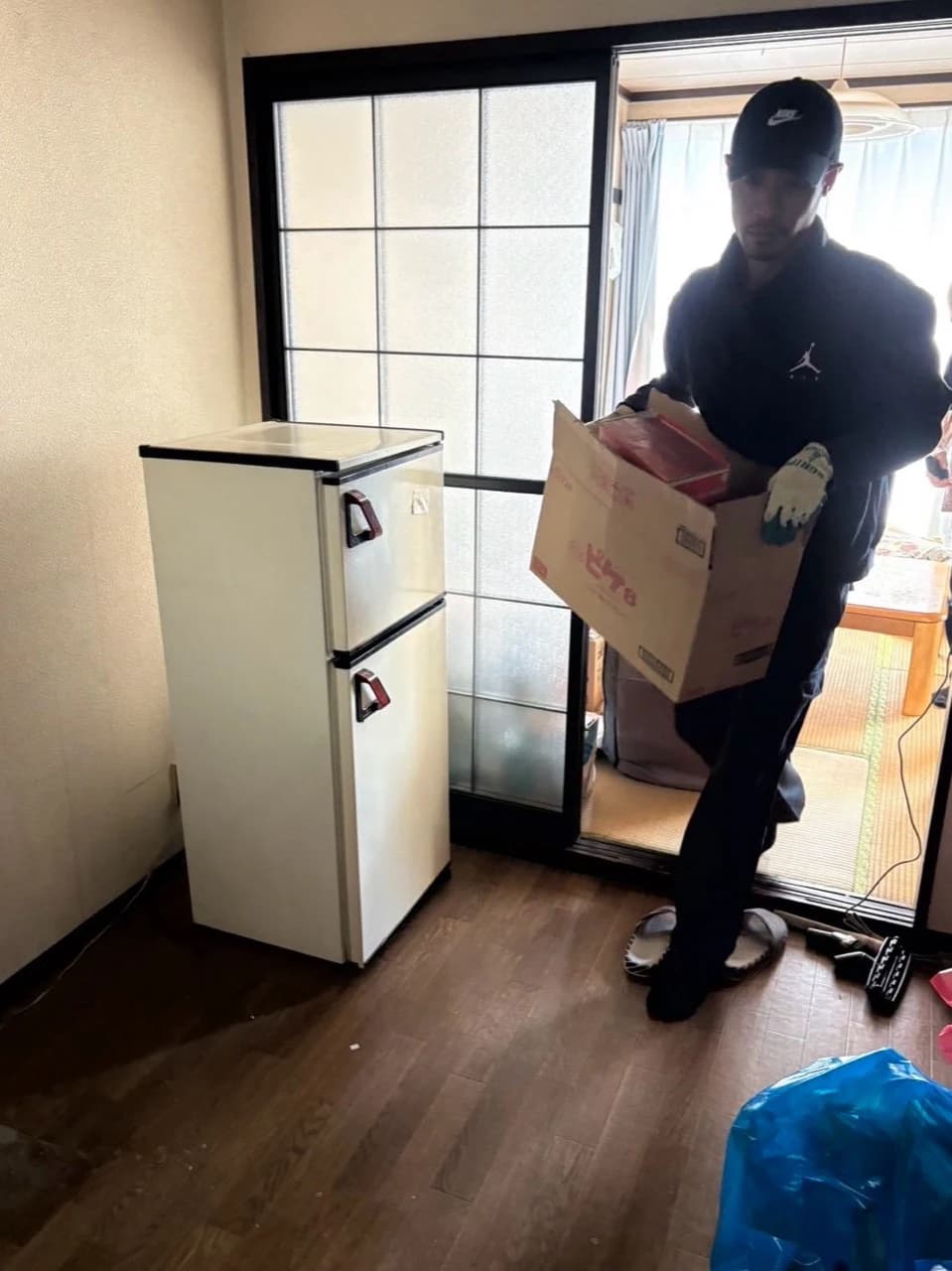 冷蔵庫のそばを通り、段ボール箱を運び出すスタッフ