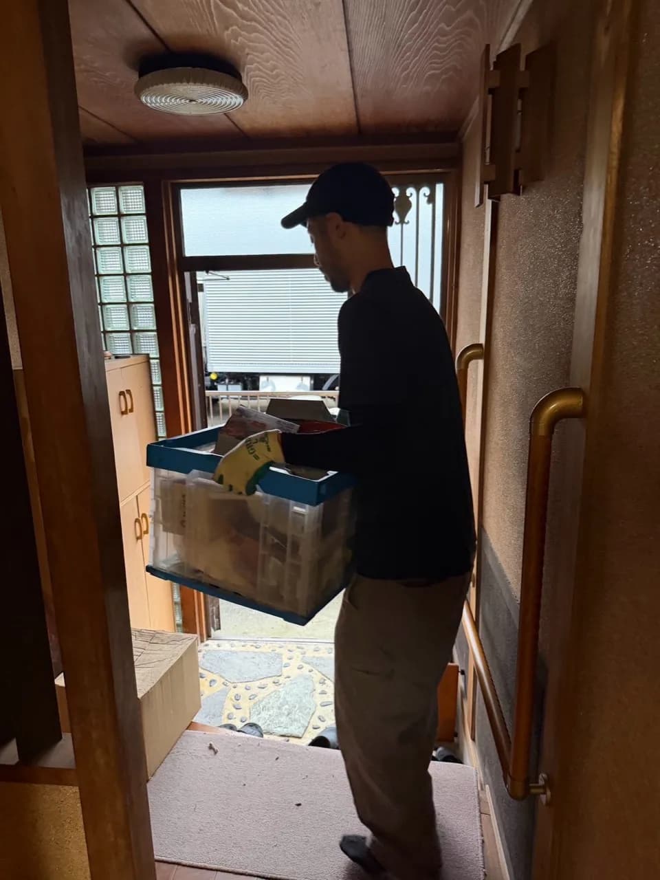 品物を入れた青い縁のケースを玄関から運び出すスタッフ
