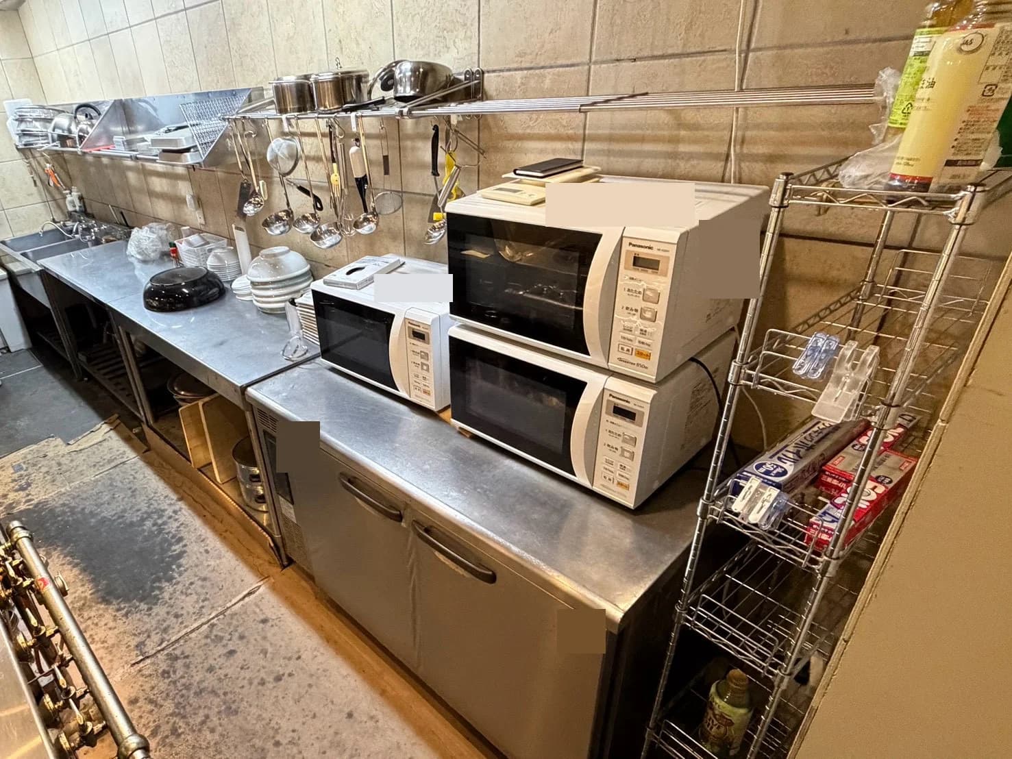 横型の冷蔵設備の上に置かれた電子レンジと、周囲の食器・調理器具