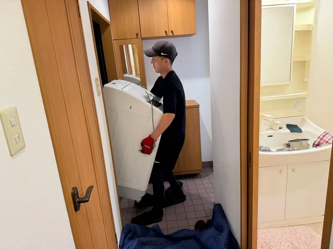 養生した床の上で洗濯機を玄関へ運ぶ様子