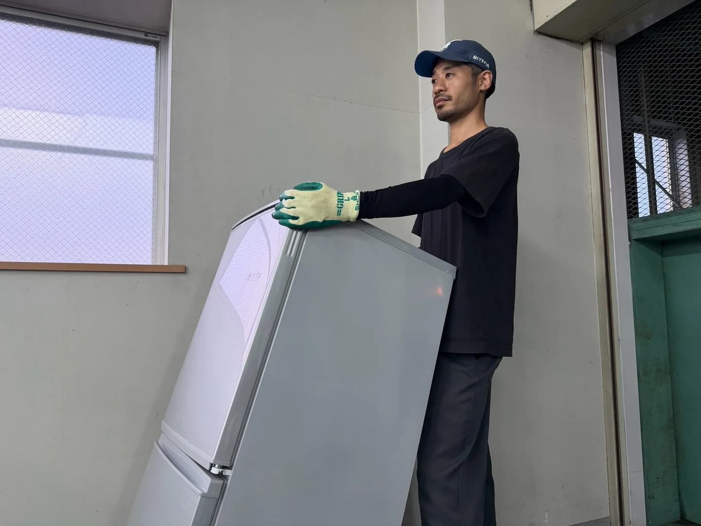 手袋を着けたスタッフが室内で銀色の冷蔵庫を支えている様子
