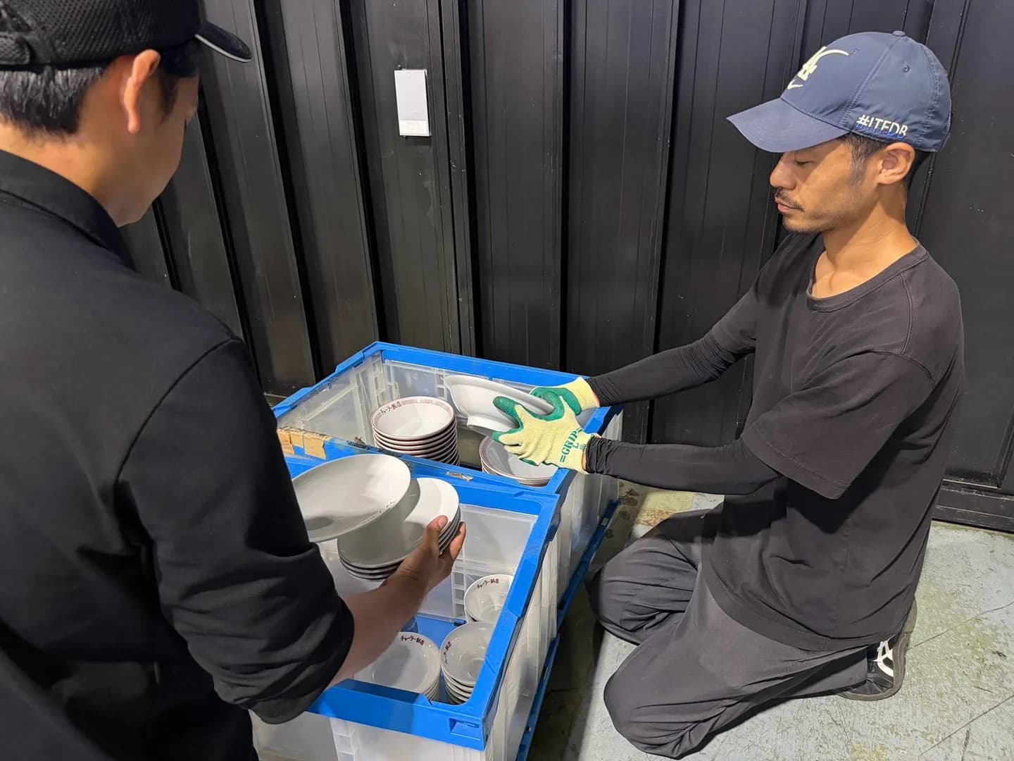 青いコンテナに入った白い食器を2人のスタッフが手に取って仕分ける様子