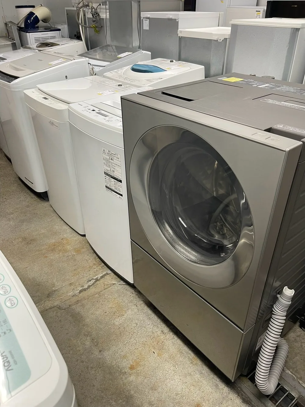 店内に並ぶ複数の縦型洗濯機と手前のドラム式洗濯機